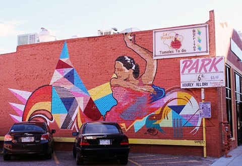 Colorful mural of woman dancing painted onto a brick wall of an older Denver establishment. 