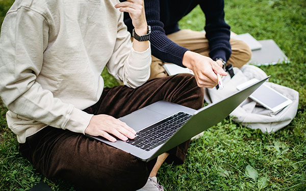 students sitting on grass working together on a laptop
