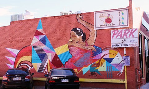 Colorful mural of woman dancing painted onto a brick wall of an older Denver establishment. 