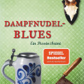 Book cover for “Dampfnudel-Blues” by Rita Falk: green patterned background, deer trophy, beer stein, cleaver, and red checkered tablecloth.